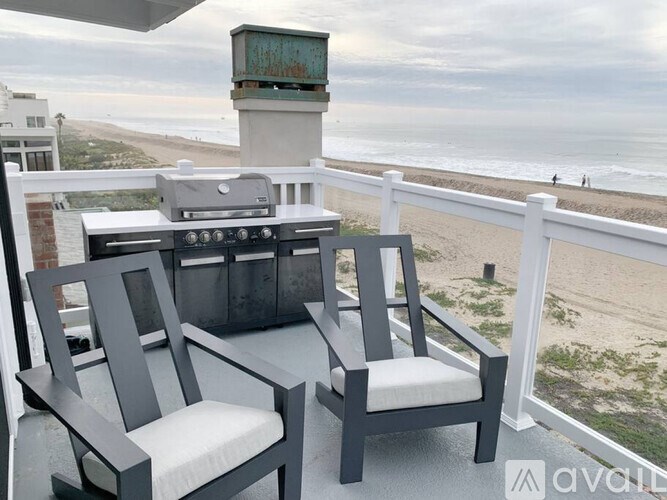 Two chairs and a table on a balcony overlooking the beach.