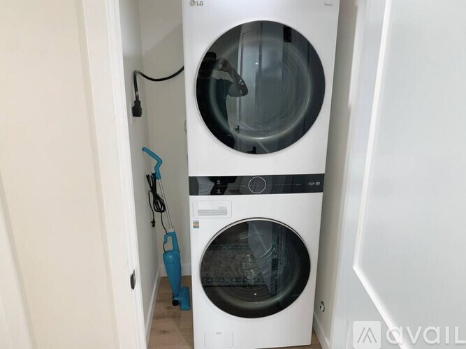 A white LG washing machine with a blue vacuum cleaner in front of it.