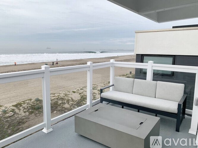 A balcony with a white couch and a coffee table overlooking the beach.
