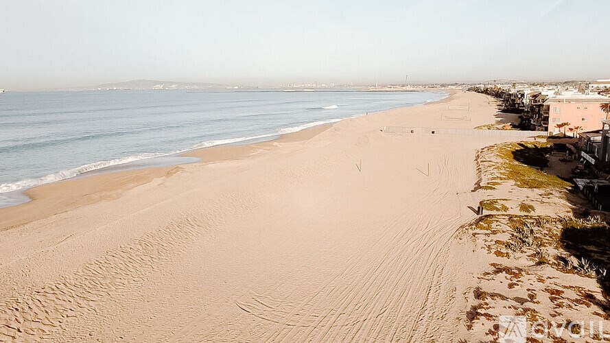 A sandy beach with buildings on the right side and the ocean in the background.