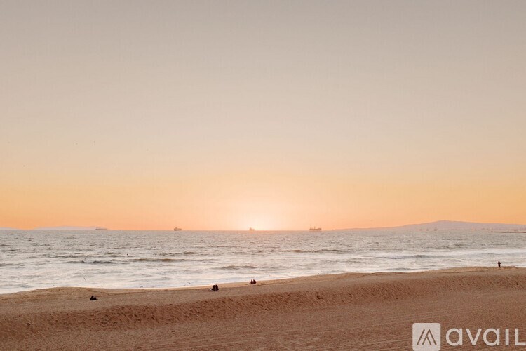 A beach at sunset with people walking along the shore.