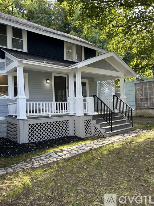 A white house with a black roof and a porch with a lattice design.