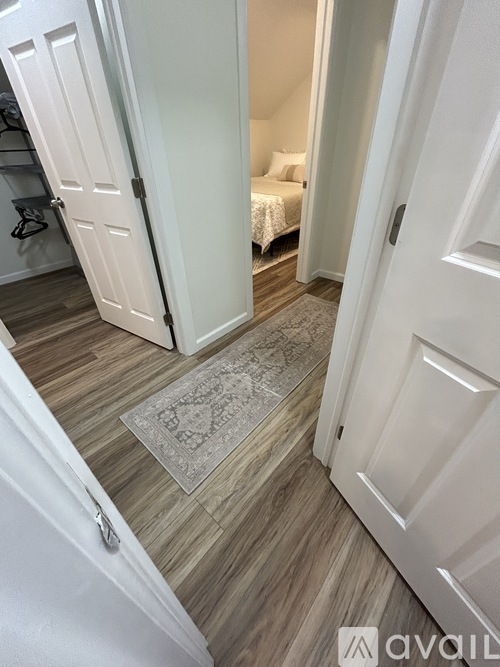 A hallway with a rug on the floor and a bedroom visible through the door.