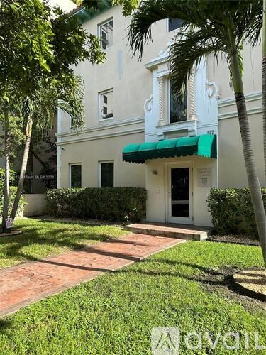 A white building with a green awning is surrounded by trees and bushes.