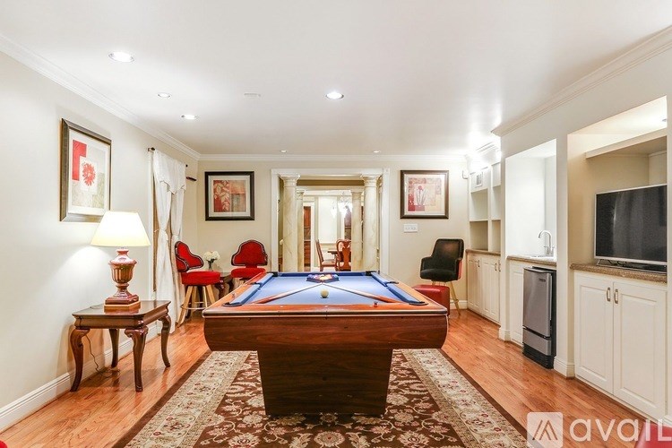 A pool table is in the middle of a room with a red chair and a lamp.