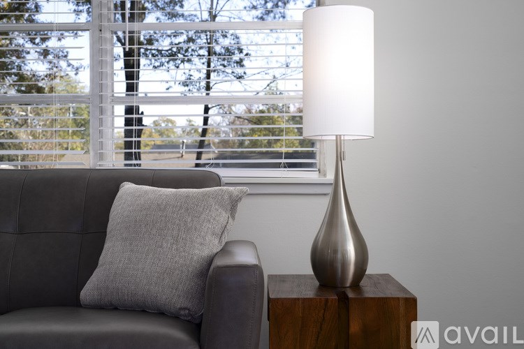 A grey couch with a grey pillow and a silver lamp on a wooden block.