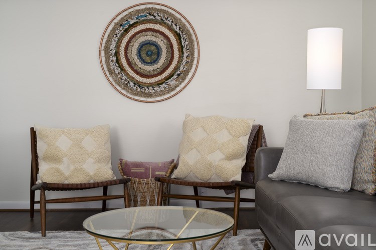 A living room with a grey couch, two chairs, and a glass table.