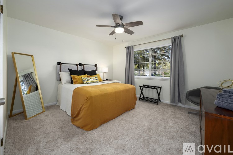 A bedroom with a bed covered in an orange sheet, a ceiling fan, and a window with a view of trees outside.