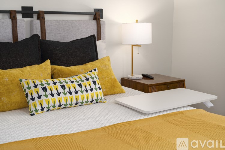 A bed with yellow and black pillows and a white lamp on a bedside table.