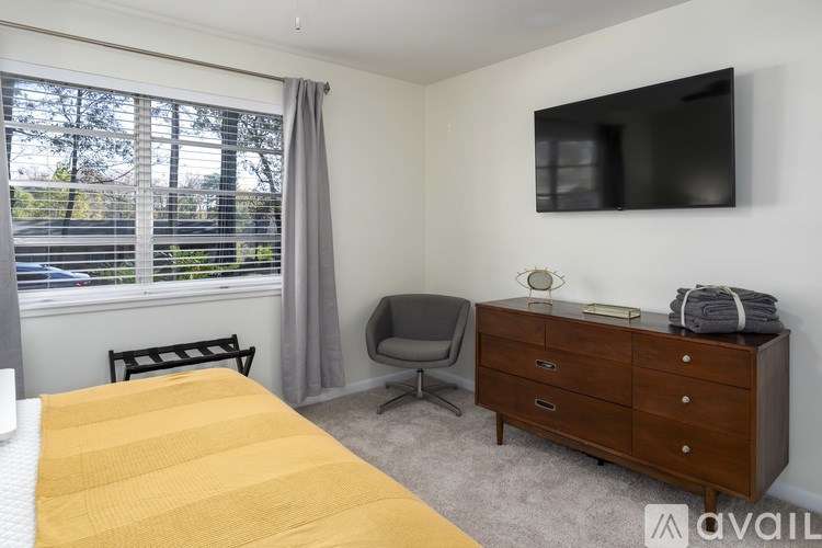 A bedroom with a bed, chair, and a cabinet with a television mounted on the wall.