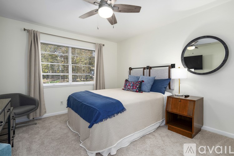 A bedroom with a bed, a chair, a ceiling fan, and a window with curtains.