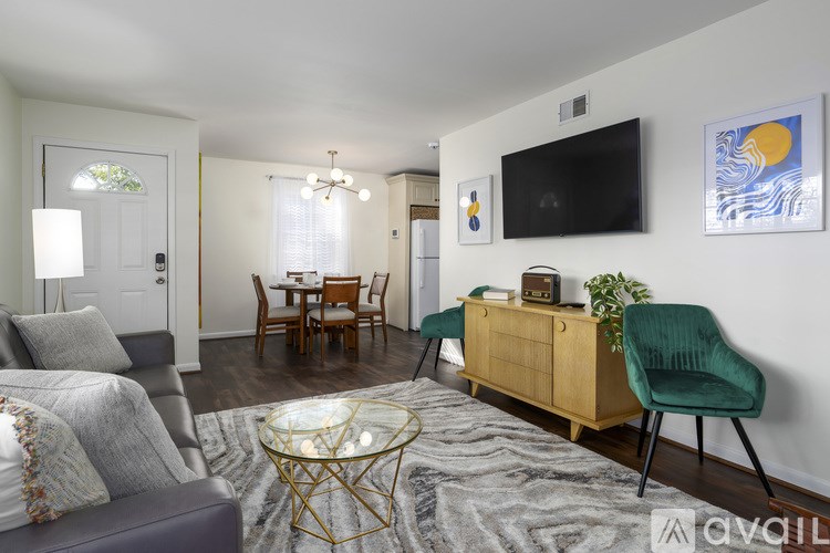 A living room with a grey couch, a glass table, a wooden cabinet, and a TV mounted on the wall.