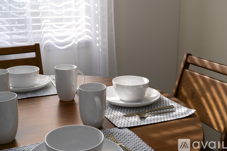 A table set with white dishes and cups with a window in the background.