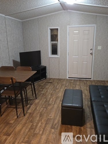 A room with a wooden floor, a white door, a black sofa, and a television.