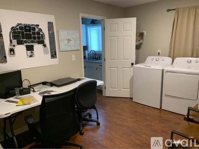 A room with a desk, chairs, and a washer and dryer.