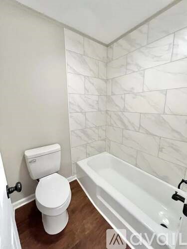 A white toilet sits next to a bathtub in a bathroom with marble tile walls.