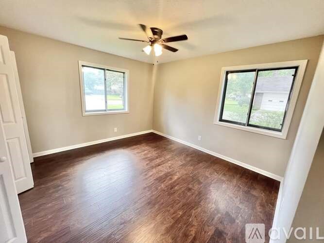 A room with a ceiling fan and two windows.