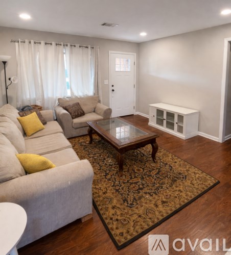 A spacious living room with hardwood floors and a kitchen area in the background.