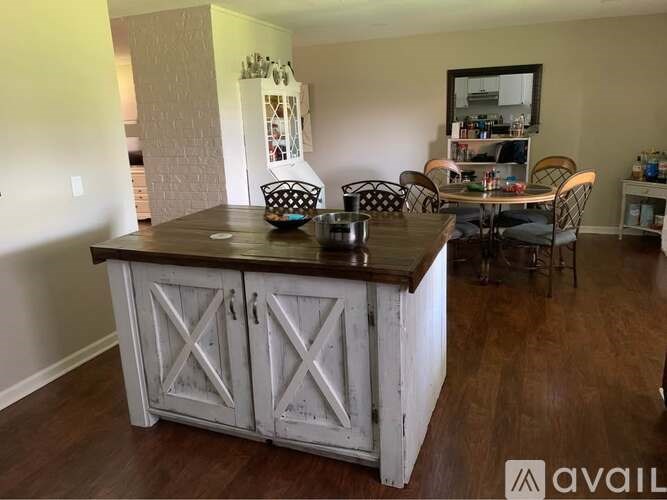A white wooden cabinet with a black countertop is in the foreground of a room with a dining table and chairs in the background.