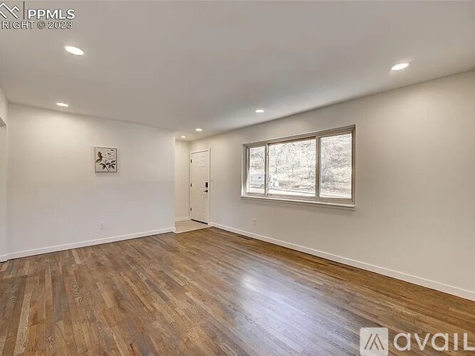 A spacious room with wooden flooring and a window letting in natural light.