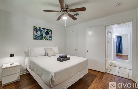 A bedroom with a white bed, a ceiling fan, and a painting on the wall.
