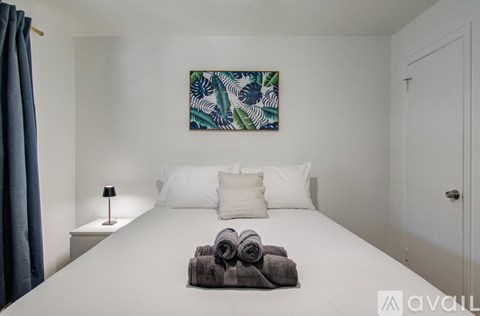 A bedroom with a white bed and a blue and green painting on the wall.