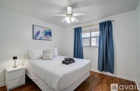 A bedroom with a white bed, blue curtains, and a ceiling fan.