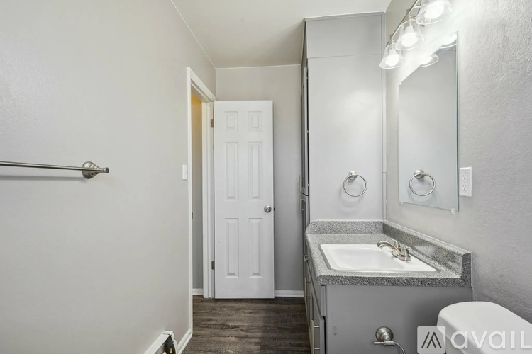 A bathroom with a sink, mirror, toilet, and a door.