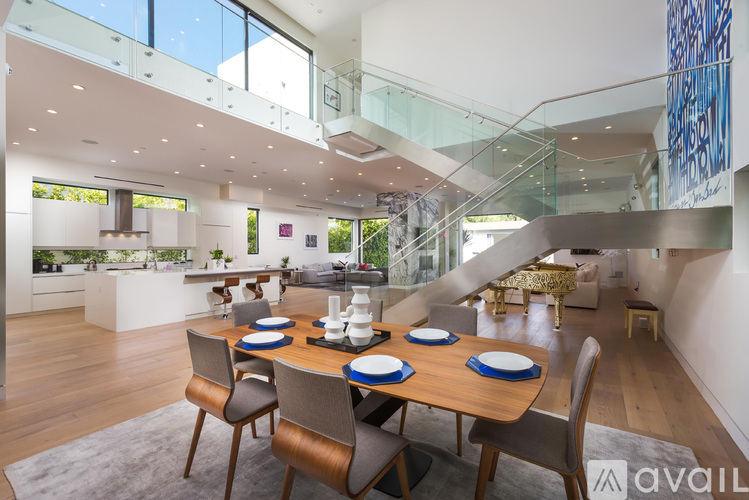 A modern dining room with a glass staircase and a wooden table set for four.