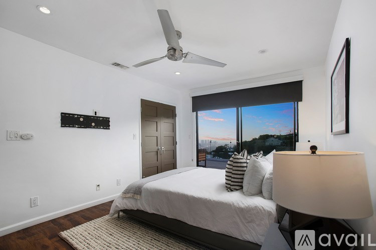 A bedroom with a large bed, a ceiling fan, and a view of the outdoors through a window.