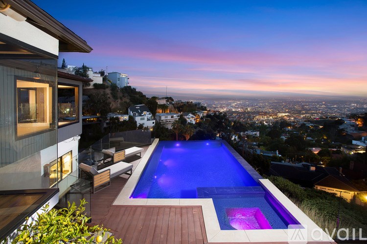 A modern house with a pool and a view of the city at dusk.