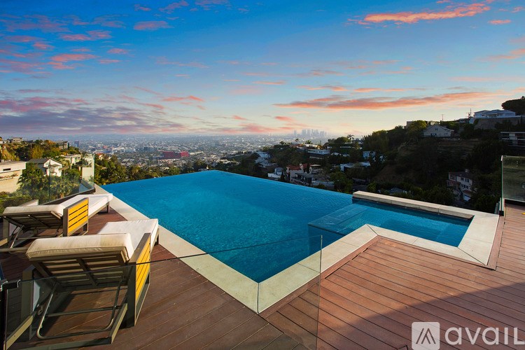 A swimming pool on a wooden deck with chairs and a city view in the background.