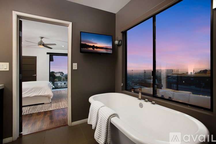 A modern bathroom with a large tub and a view of the city at dusk.