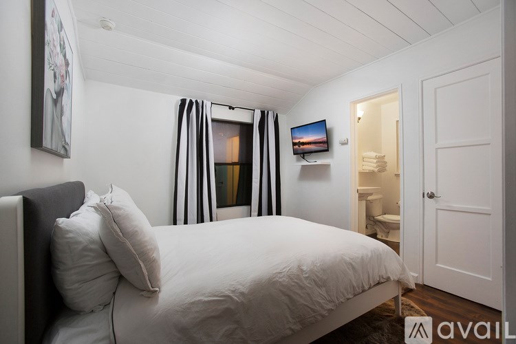 A bedroom with a bed, a mirror, a window with curtains, and a small TV mounted on the wall.