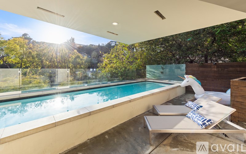 A modern outdoor pool area with a sun lounger and a view of the trees.