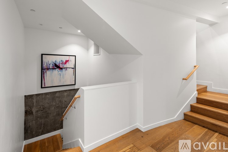 A staircase with wooden steps and a white wall with a painting hanging on it.