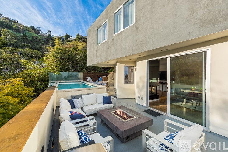 A modern house with a pool and a patio with white chairs and a fire pit.