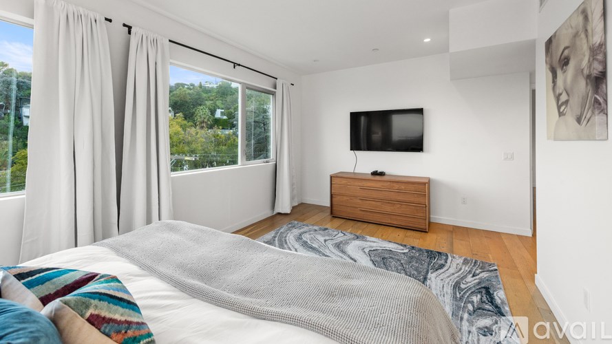 A bedroom with a bed, a television, and a window with curtains.