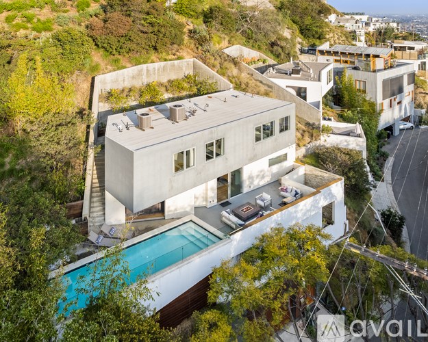 A modern house with a pool is surrounded by trees and is for sale.