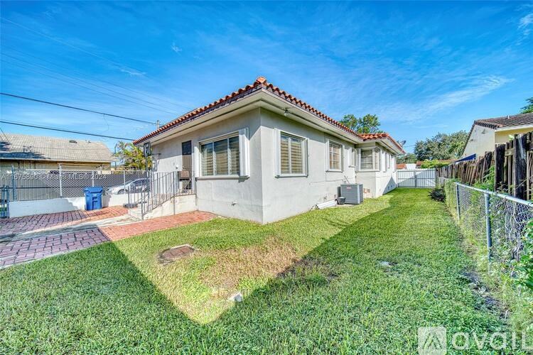 A small house with a red tile roof and a fenced yard.