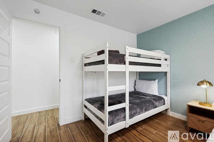 A white bunk bed with a grey mattress is in a room with a white door and wooden floor.