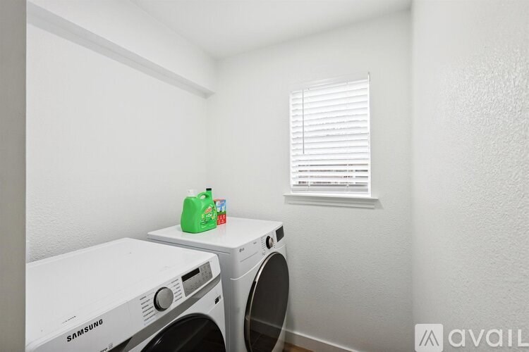 A white Samsung washing machine sits next to a white dryer in a small laundry room.
