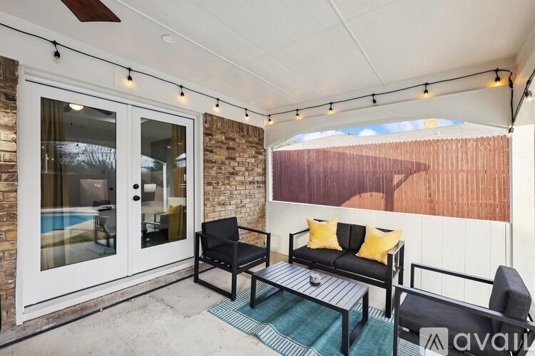 A patio with a black couch, yellow pillows, and a glass door leading to a pool.
