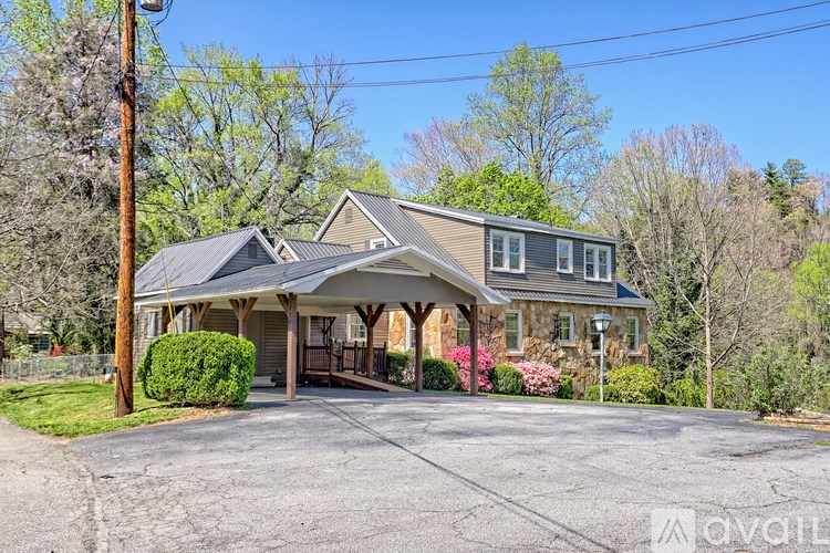 A house with a grey roof and a porch surrounded by greenery.