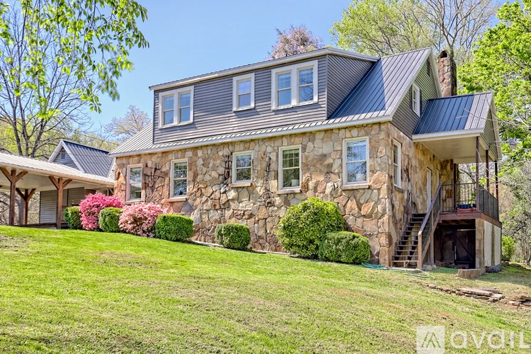 A house with a stone exterior and a grey roof is surrounded by greenery.