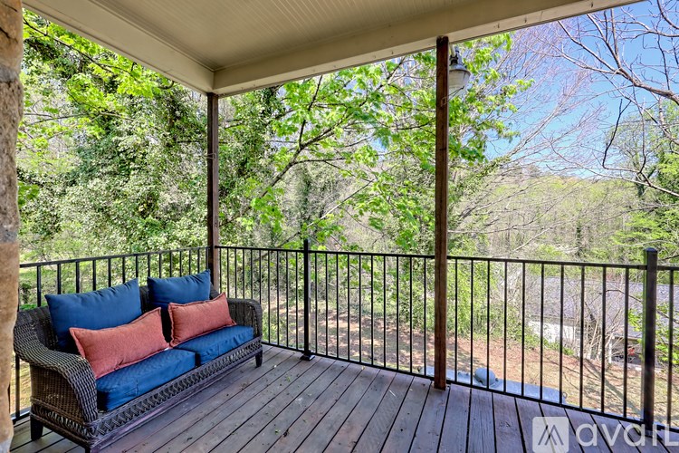 A balcony with a blue couch and pillows overlooking a wooded area.