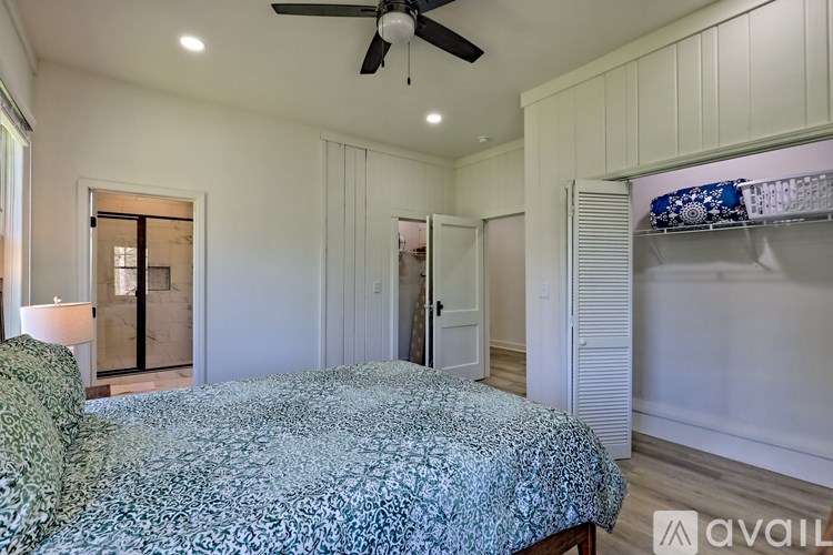 A bedroom with a bed, a ceiling fan, and a window with a view of a balcony.