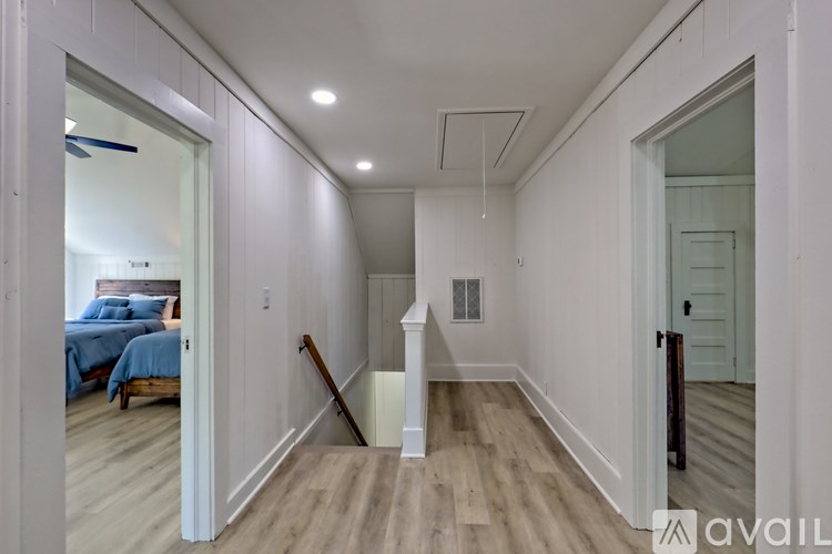 A room with a wooden floor and white walls, with a bed in the background.