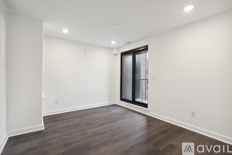 A spacious room with wooden flooring and a sliding glass door.