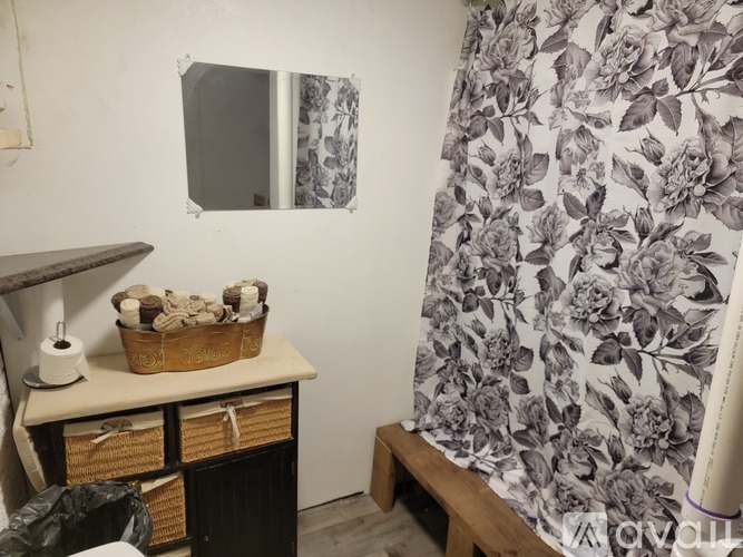 A bathroom with a floral shower curtain and a mirror above a counter with a basket of towels on it.